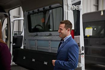 A smiling man in a blue suit is standing in front of an open van